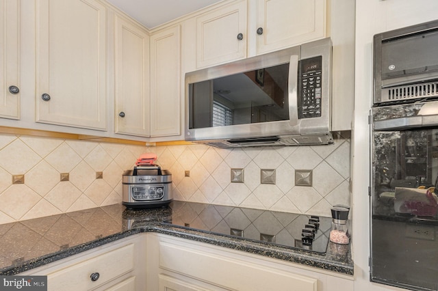 kitchen with dark stone counters, decorative backsplash, cream cabinetry, and black appliances