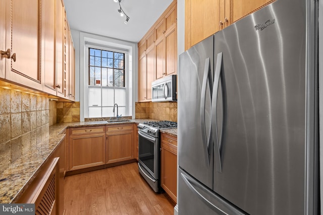 kitchen with stainless steel appliances, light stone countertops, sink, and light hardwood / wood-style flooring