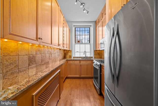 kitchen featuring sink, light hardwood / wood-style flooring, appliances with stainless steel finishes, tasteful backsplash, and light stone countertops