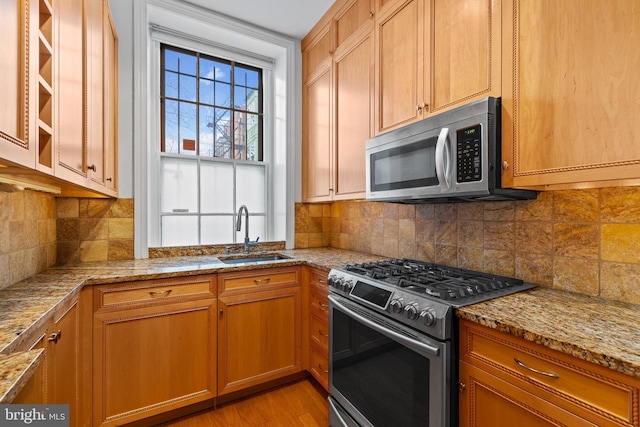 kitchen with sink, light stone counters, stainless steel appliances, light hardwood / wood-style floors, and backsplash