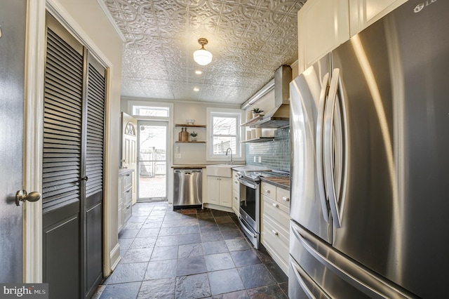 kitchen featuring appliances with stainless steel finishes, wall chimney range hood, backsplash, open shelves, and an ornate ceiling