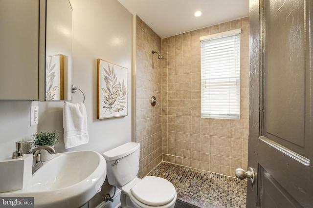 bathroom with tiled shower, a sink, and toilet