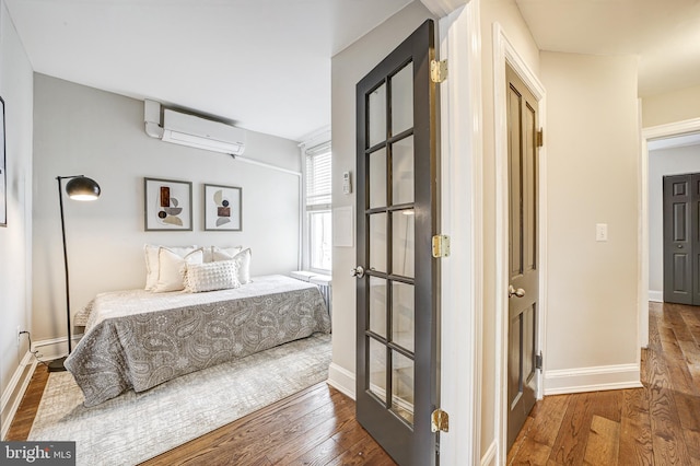 bedroom featuring hardwood / wood-style floors, baseboards, and an AC wall unit