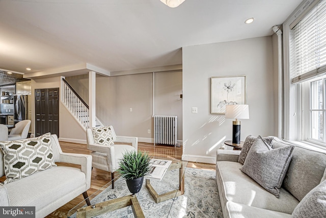 living area with recessed lighting, wood finished floors, baseboards, stairs, and radiator heating unit