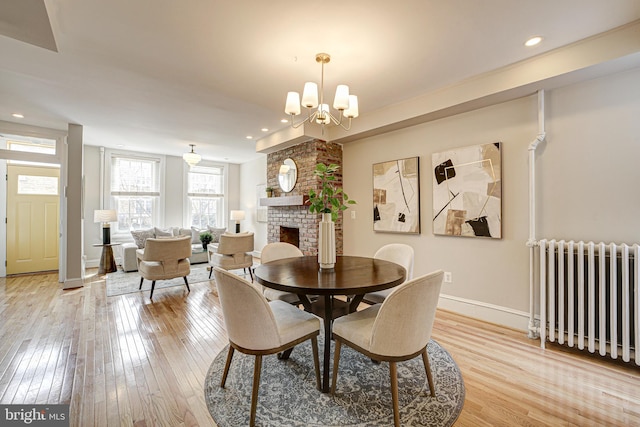 dining space with a chandelier, light wood-type flooring, radiator, and a fireplace