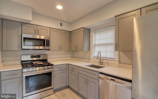 kitchen featuring gray cabinets, light stone countertops, appliances with stainless steel finishes, and sink