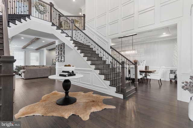 staircase with hardwood / wood-style flooring, ornamental molding, beam ceiling, and a high ceiling