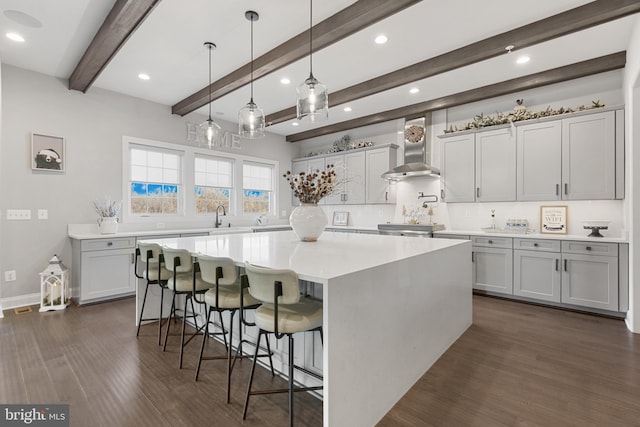 kitchen with a breakfast bar, dark hardwood / wood-style flooring, hanging light fixtures, a large island, and wall chimney range hood