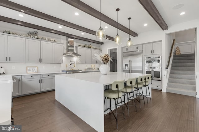 kitchen featuring a spacious island, stainless steel appliances, a kitchen breakfast bar, and wall chimney range hood