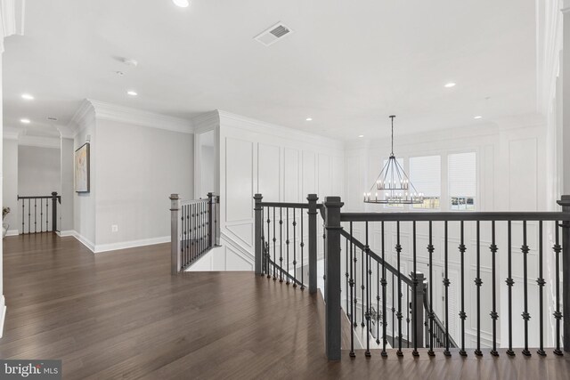 hallway with dark wood-type flooring, ornamental molding, and a chandelier