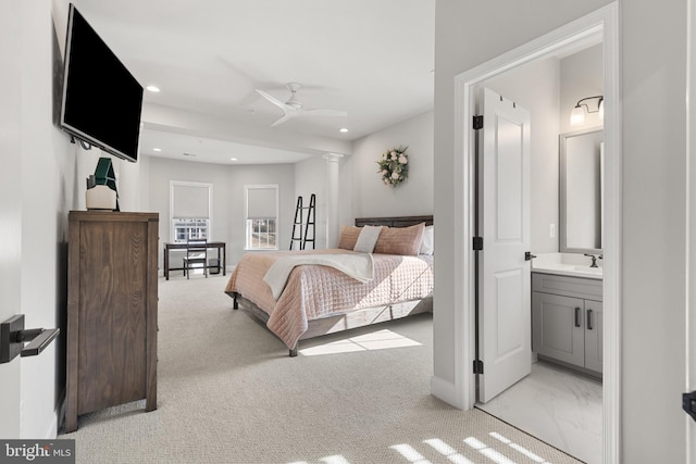 bedroom with connected bathroom, sink, light colored carpet, and ornate columns