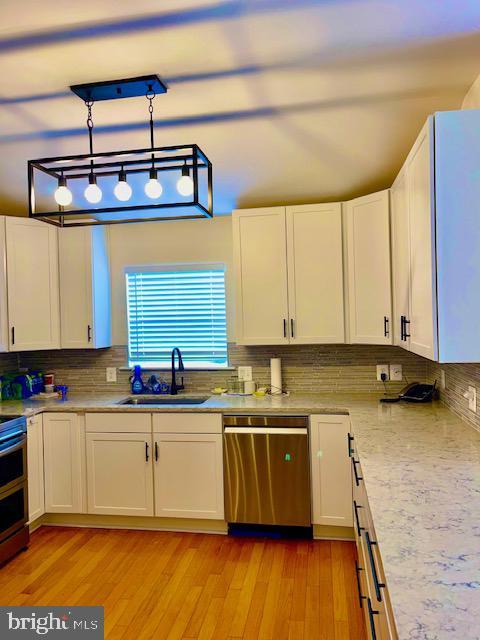 kitchen featuring pendant lighting, sink, dishwasher, white cabinetry, and light wood-type flooring