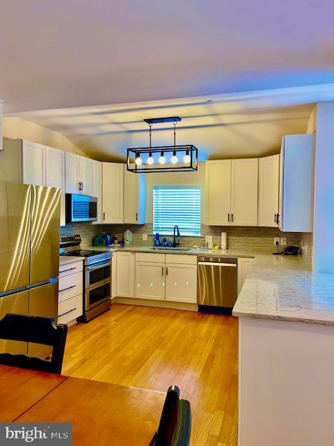 kitchen with appliances with stainless steel finishes, white cabinetry, sink, hanging light fixtures, and light stone countertops