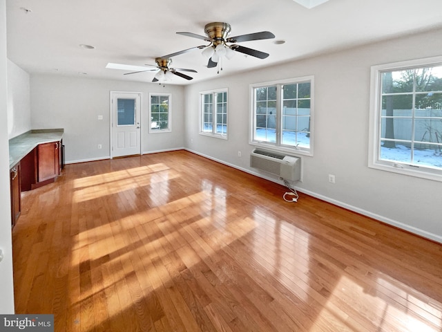 unfurnished living room with baseboards, a wall mounted AC, light wood-type flooring, and a healthy amount of sunlight