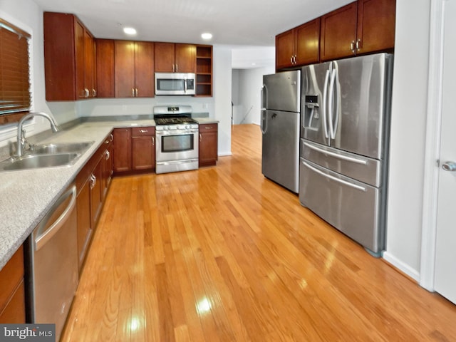 kitchen featuring appliances with stainless steel finishes, light countertops, light wood-style floors, open shelves, and a sink