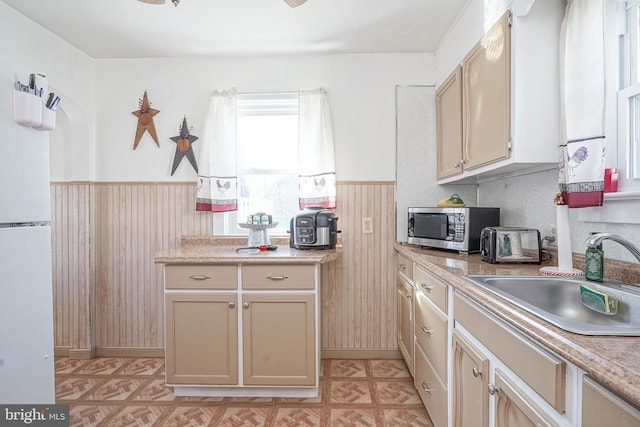 kitchen featuring light countertops, stainless steel microwave, wainscoting, a sink, and wooden walls