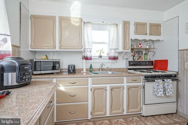 kitchen featuring white range with gas cooktop, stainless steel microwave, light countertops, and a sink