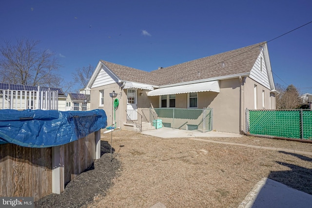 rear view of property featuring roof with shingles, fence, and stucco siding