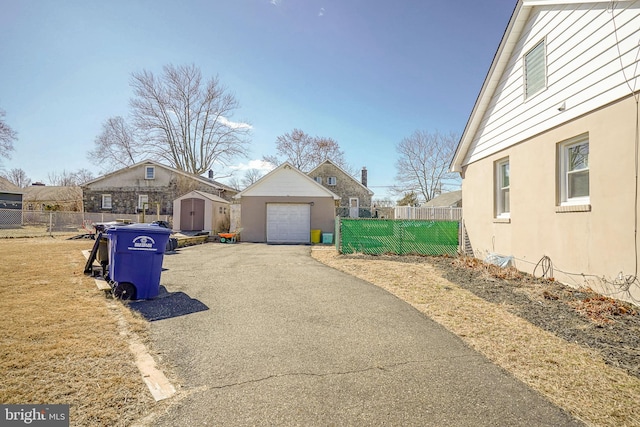 view of front of property featuring an outdoor structure, fence, a detached garage, driveway, and stucco siding