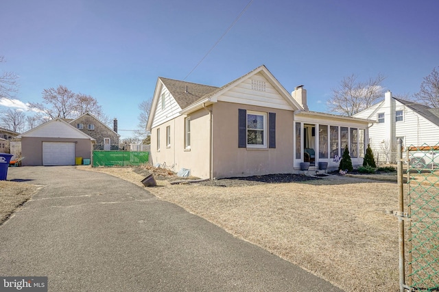 view of front facade featuring a garage, driveway, a chimney, an outbuilding, and fence