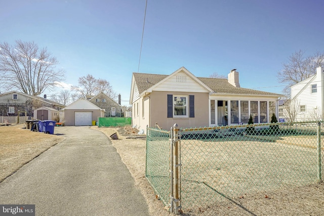 view of front of home with driveway, a detached garage, a chimney, fence, and an outdoor structure