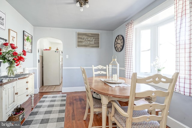 dining space featuring arched walkways, dark wood-style flooring, and baseboards