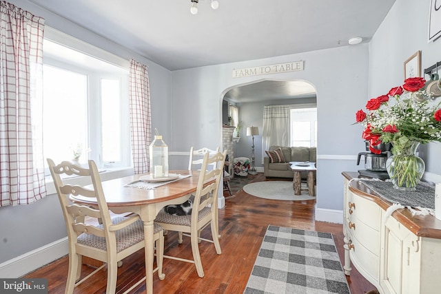 dining area featuring a wealth of natural light, arched walkways, dark wood-style flooring, and baseboards