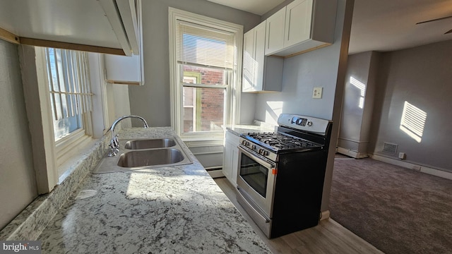 kitchen with stainless steel range with gas cooktop, sink, white cabinets, and light stone counters