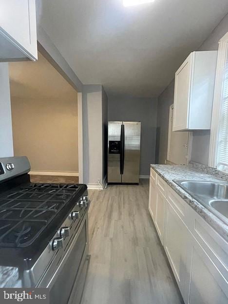 kitchen with sink, stainless steel appliances, light stone counters, white cabinets, and light wood-type flooring