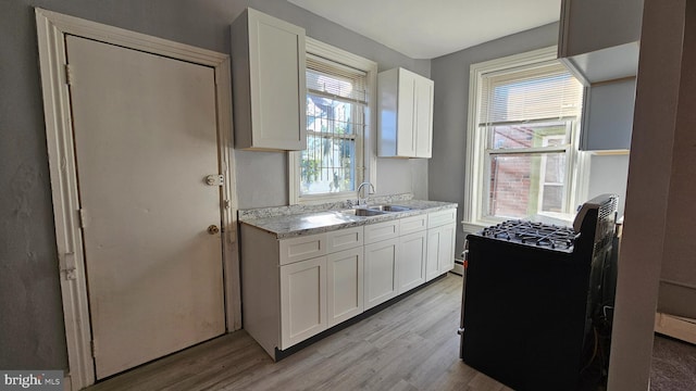 kitchen with sink, white cabinets, stove, light stone counters, and light wood-type flooring