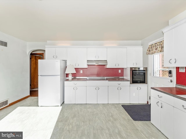 kitchen with white fridge, stainless steel oven, white cabinets, and decorative backsplash