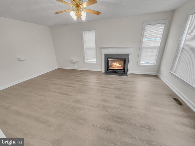 unfurnished living room with a fireplace with flush hearth, wood finished floors, visible vents, and baseboards