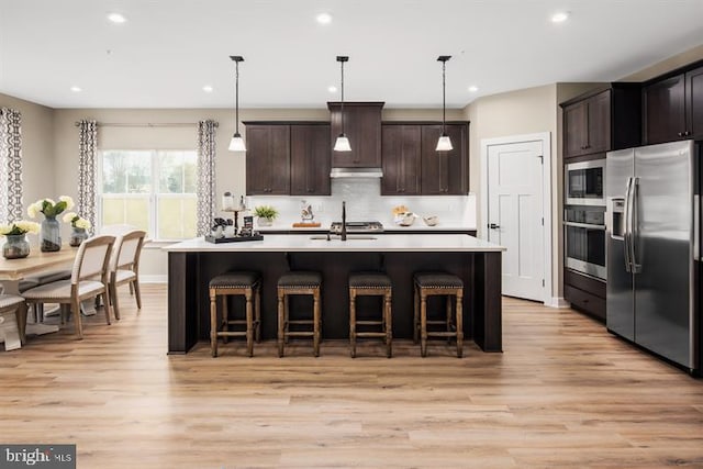 kitchen featuring dark brown cabinetry, stainless steel appliances, decorative light fixtures, and an island with sink