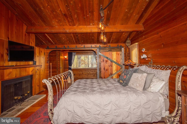 bedroom with wood ceiling, beam ceiling, a barn door, and wood walls