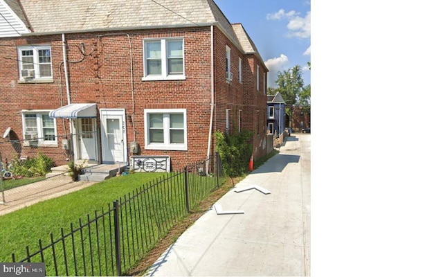 view of front facade with a fenced front yard, a high end roof, a front lawn, and brick siding