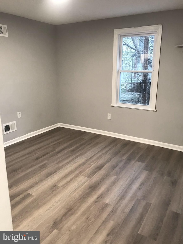 spare room featuring dark wood-style floors, visible vents, and baseboards