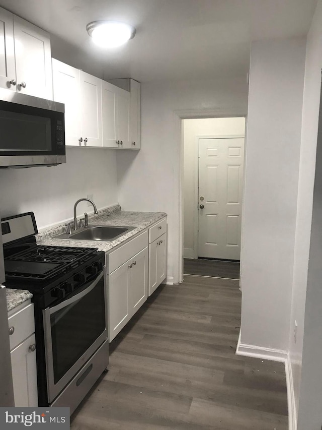 kitchen featuring light stone counters, stainless steel appliances, a sink, white cabinetry, and dark wood finished floors