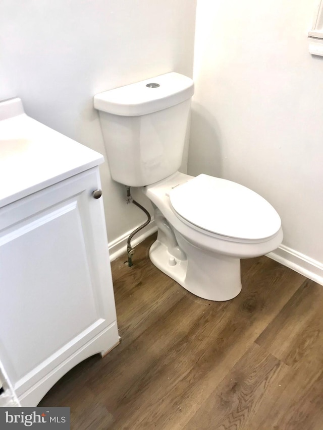 half bathroom featuring wood finished floors, vanity, toilet, and baseboards