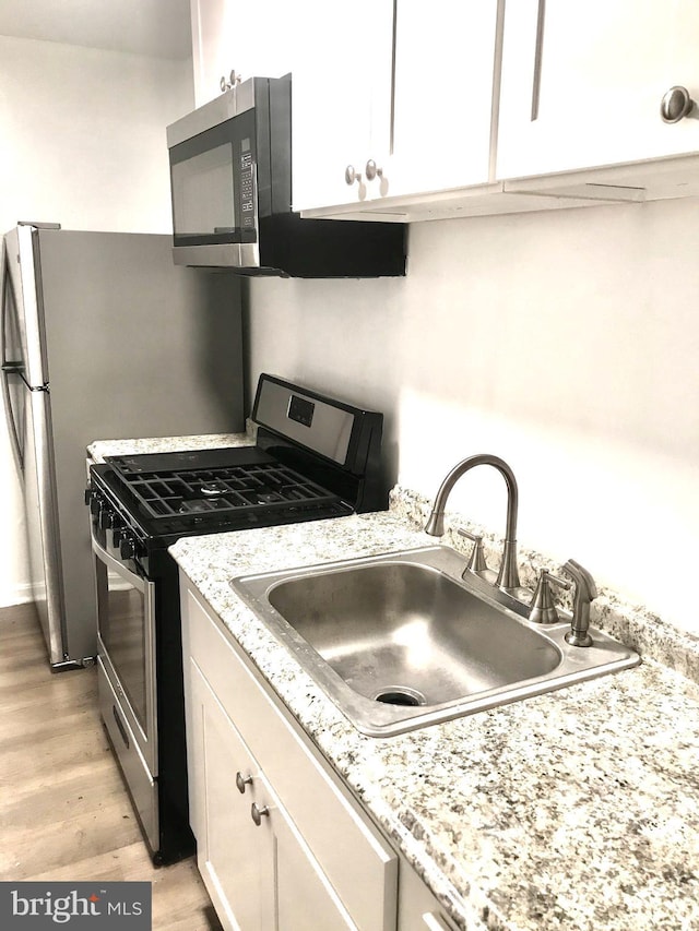 kitchen featuring light stone counters, a sink, white cabinets, appliances with stainless steel finishes, and light wood-type flooring