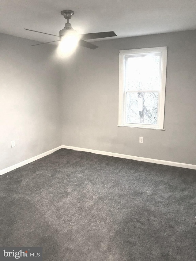 spare room featuring dark colored carpet, ceiling fan, and baseboards