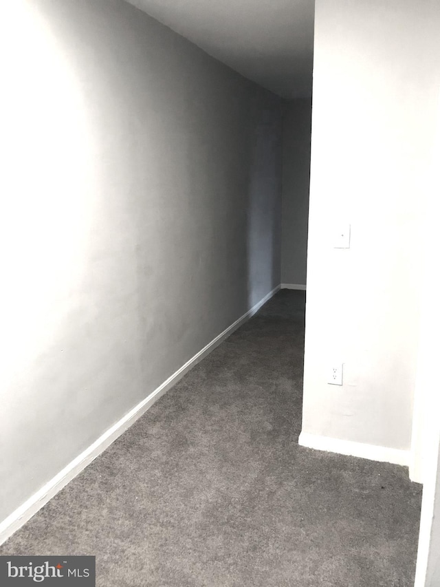 unfurnished room featuring dark colored carpet and baseboards