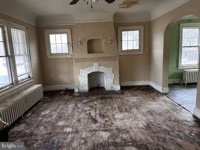 unfurnished living room with a brick fireplace, radiator heating unit, dark hardwood / wood-style floors, and ceiling fan