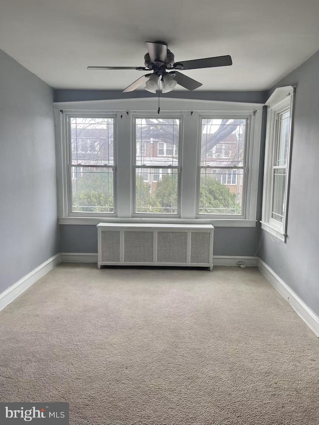 unfurnished room featuring ceiling fan, light colored carpet, and radiator