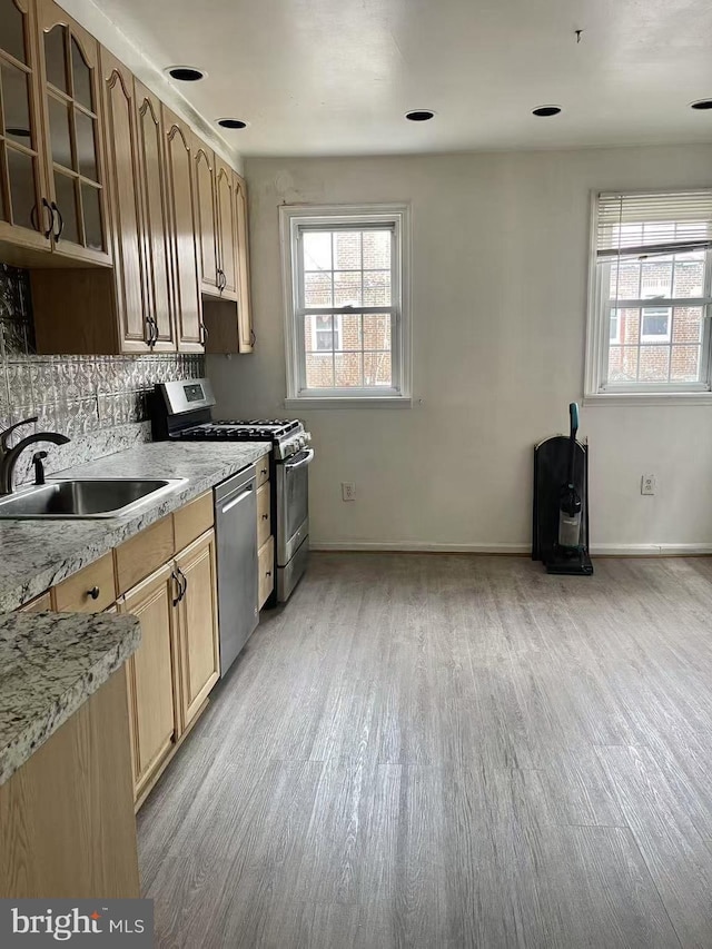 kitchen with appliances with stainless steel finishes, sink, backsplash, and light wood-type flooring