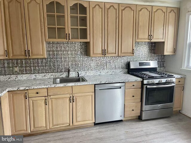 kitchen with sink, light stone counters, stainless steel appliances, light hardwood / wood-style floors, and backsplash