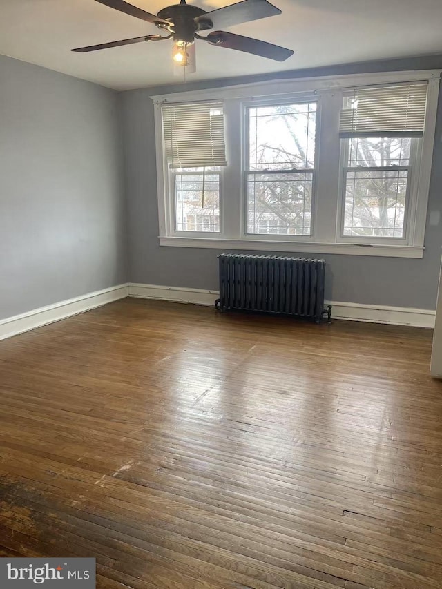 empty room with ceiling fan, dark hardwood / wood-style floors, and radiator