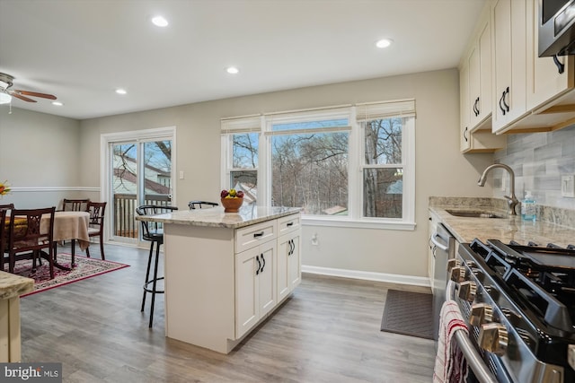 kitchen featuring appliances with stainless steel finishes, a center island, light stone counters, white cabinets, and a kitchen bar