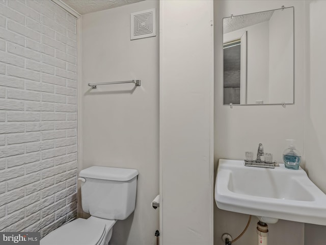 bathroom with brick wall, sink, a textured ceiling, and toilet