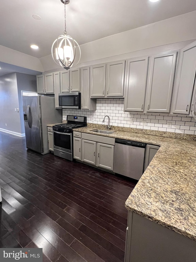 kitchen featuring dark wood-style flooring, a sink, decorative backsplash, hanging light fixtures, and appliances with stainless steel finishes