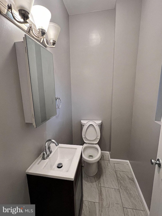 half bathroom featuring marble finish floor, toilet, vanity, and baseboards